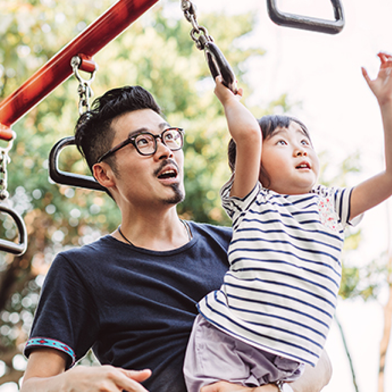 adult male holding a toddler on the monkey bars