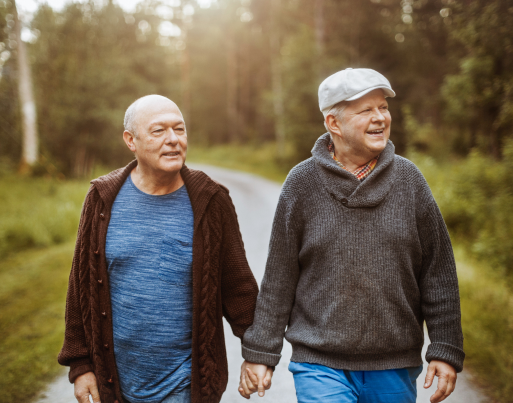 2 older gentleman holding hands walking in a forest.