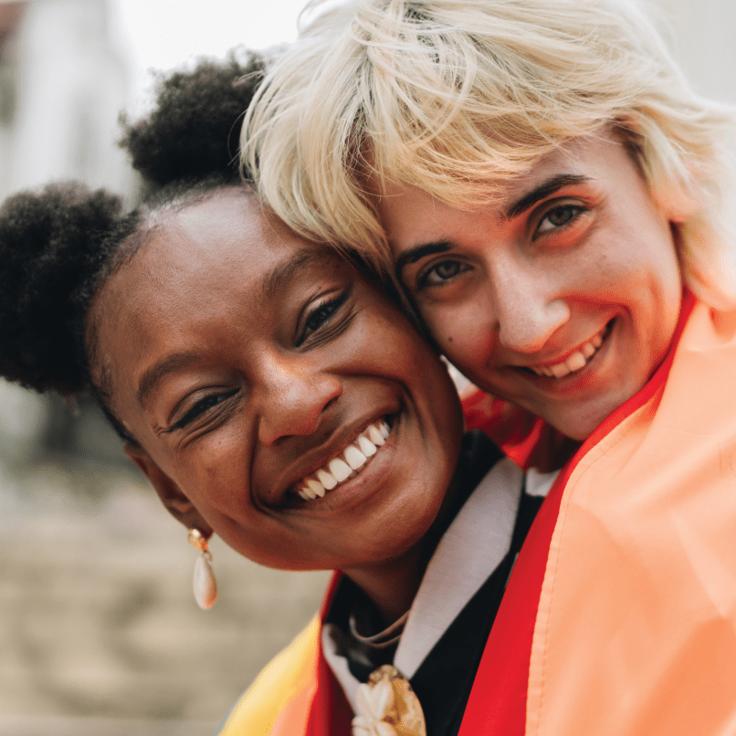 2 middle-aged women smiling to the camera embracing each other.