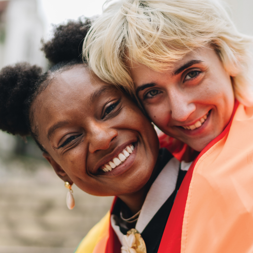 2 middle-aged women smiling to the camera embracing each other.
