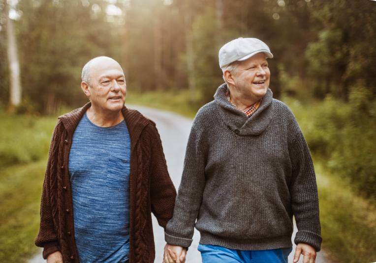 2 older gentleman holding hands walking in a forest.