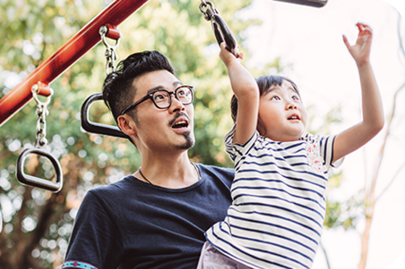 adult male holding a toddler on the monkey bars