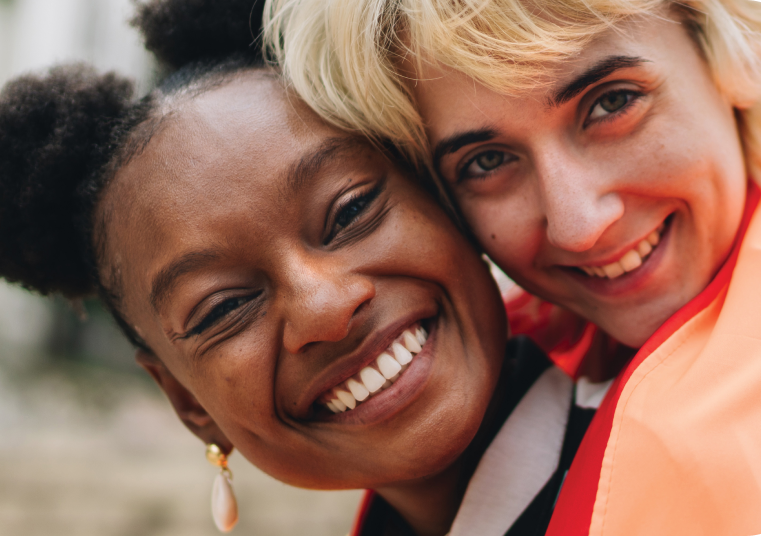 2 middle-aged women smiling to the camera embracing each other.