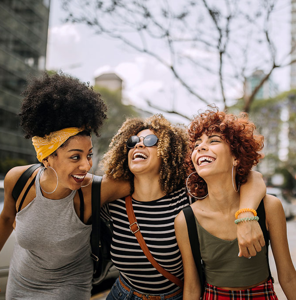 3 smiling middle-aged women stood together wrapped up for a cold day on a pier.