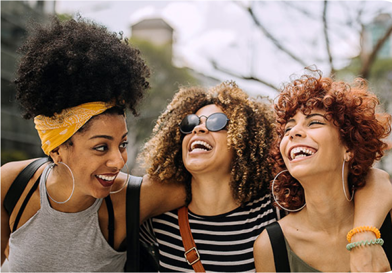3 smiling middle-aged women stood together wrapped up for a cold day on a pier.